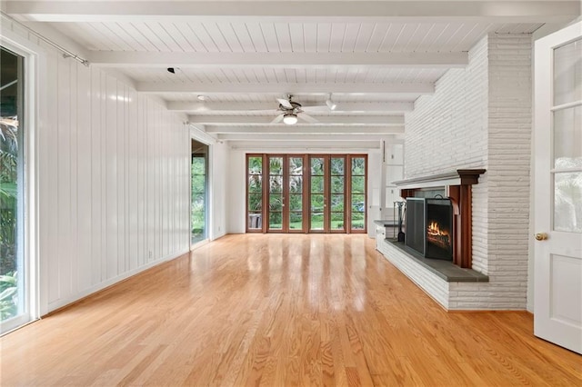 unfurnished living room with beam ceiling, a brick fireplace, light wood-type flooring, and ceiling fan