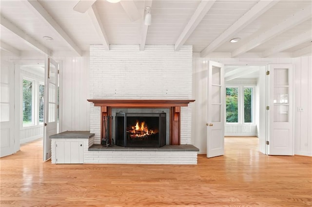 unfurnished living room featuring light hardwood / wood-style floors, a brick fireplace, beamed ceiling, and a healthy amount of sunlight