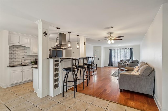 kitchen with tasteful backsplash, light wood-type flooring, white cabinets, hanging light fixtures, and island exhaust hood