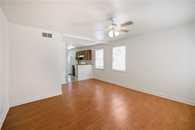 unfurnished living room with ceiling fan, visible vents, baseboards, and wood finished floors