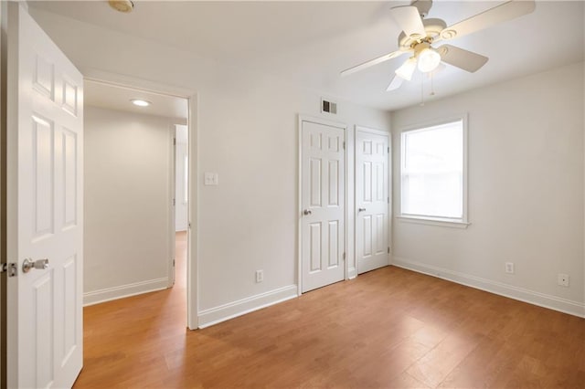 unfurnished bedroom featuring two closets, hardwood / wood-style floors, and ceiling fan