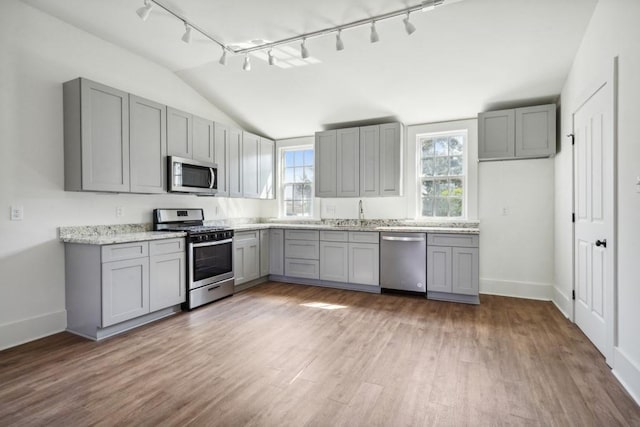 kitchen with gray cabinets, stainless steel appliances, light stone countertops, hardwood / wood-style flooring, and lofted ceiling