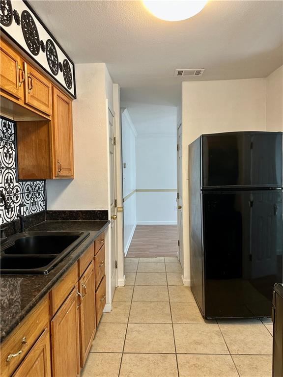 kitchen featuring light tile patterned flooring, black refrigerator, sink, dark stone counters, and a textured ceiling