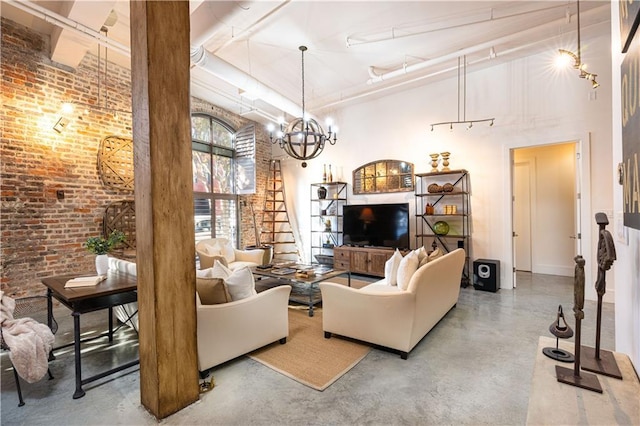 living room featuring an inviting chandelier, brick wall, a towering ceiling, concrete floors, and track lighting