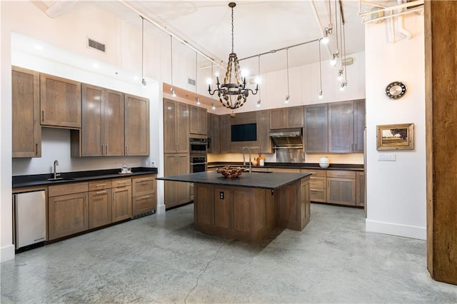 kitchen featuring sink, stainless steel appliances, hanging light fixtures, a high ceiling, and a kitchen island with sink