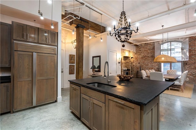 kitchen with paneled built in refrigerator, sink, a kitchen island with sink, and brick wall