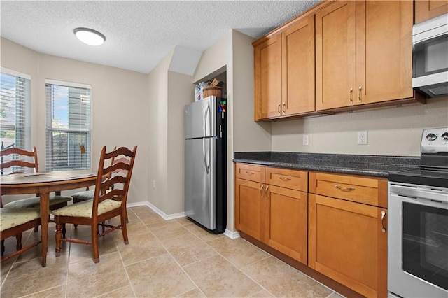 kitchen featuring light tile patterned flooring, dark stone countertops, a textured ceiling, and stainless steel appliances