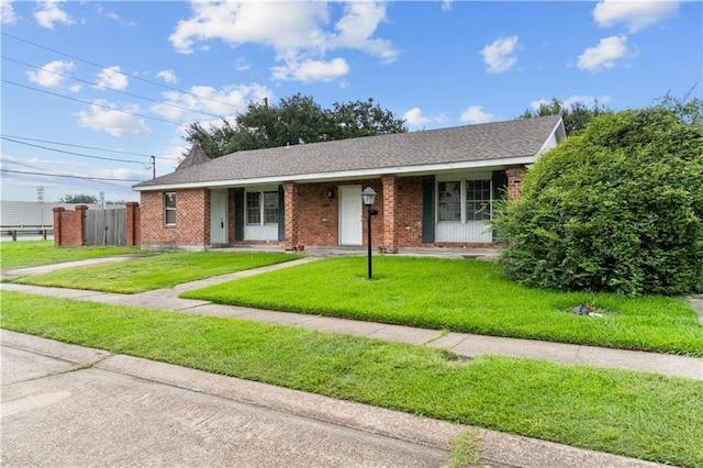 ranch-style home featuring fence, a front yard, a shingled roof, and brick siding