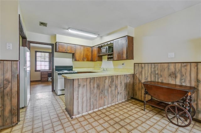 kitchen with white appliances, wooden walls, sink, and kitchen peninsula