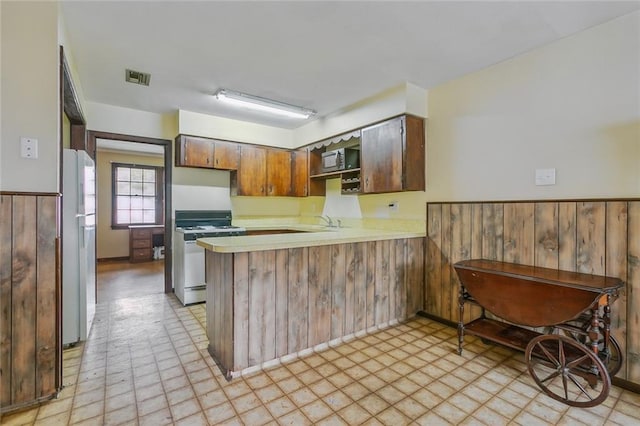kitchen with visible vents, range with gas cooktop, a peninsula, light countertops, and freestanding refrigerator