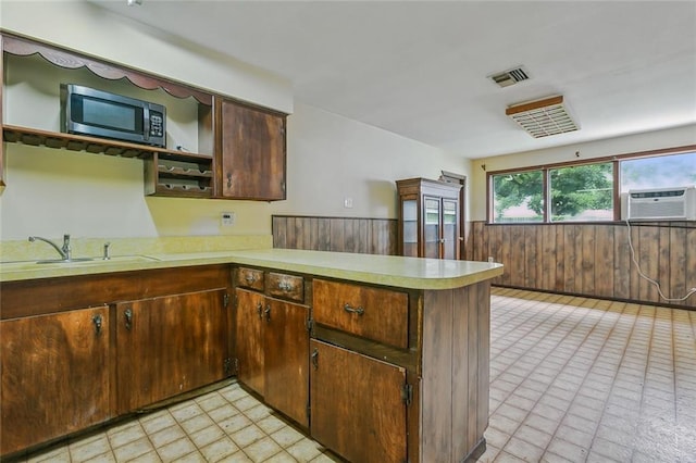 kitchen with a wall unit AC, kitchen peninsula, dark brown cabinetry, and sink