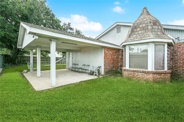 rear view of property with a lawn, brick siding, fence, and a patio area