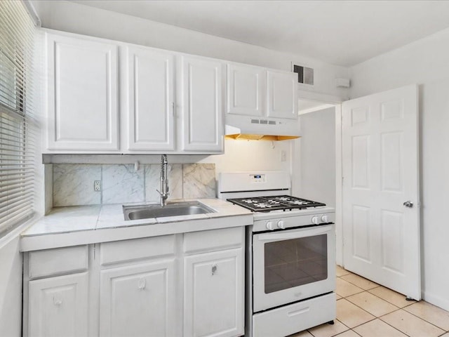 kitchen featuring custom exhaust hood, white cabinets, backsplash, white gas stove, and sink