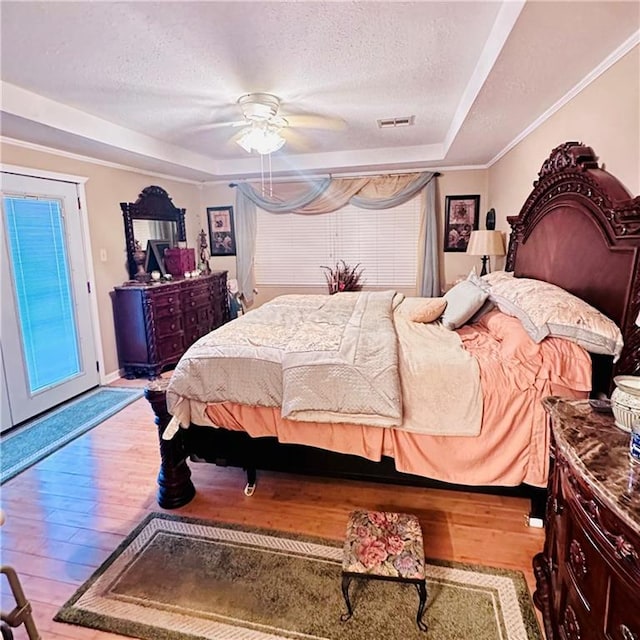 bedroom with a raised ceiling, a textured ceiling, ceiling fan, and hardwood / wood-style floors