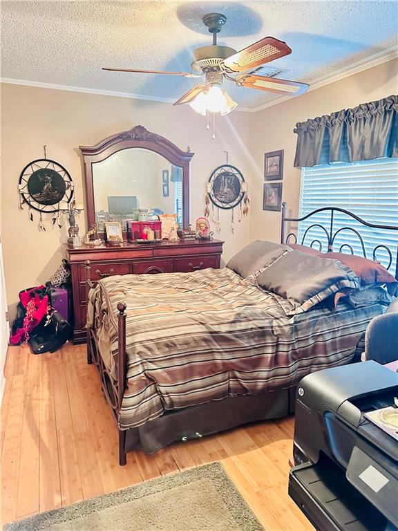 bedroom with a textured ceiling, ceiling fan, hardwood / wood-style floors, and crown molding