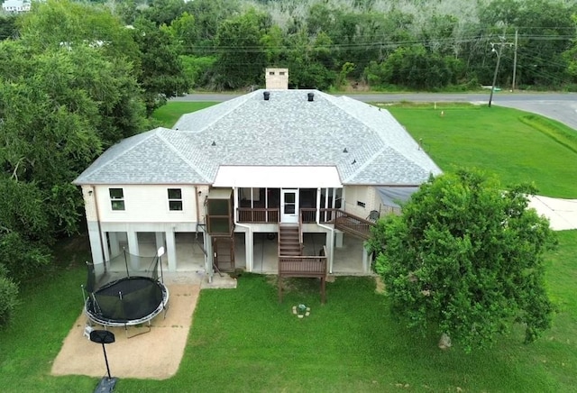 rear view of property with a lawn, roof with shingles, a trampoline, and stairway