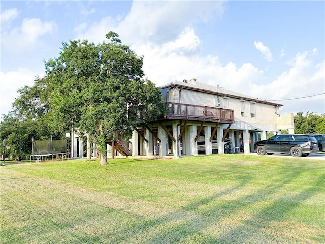 rear view of house featuring a lawn, a deck, stairs, and a trampoline