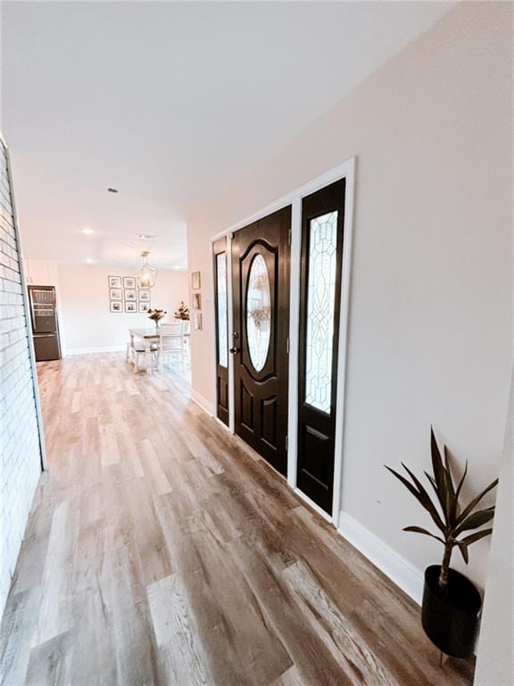 foyer with baseboards, wood finished floors, and a notable chandelier