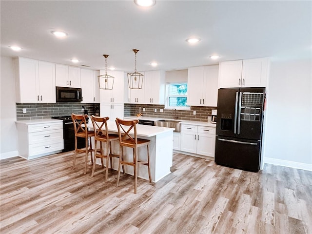 kitchen with a kitchen island, light hardwood / wood-style flooring, white cabinetry, and black appliances