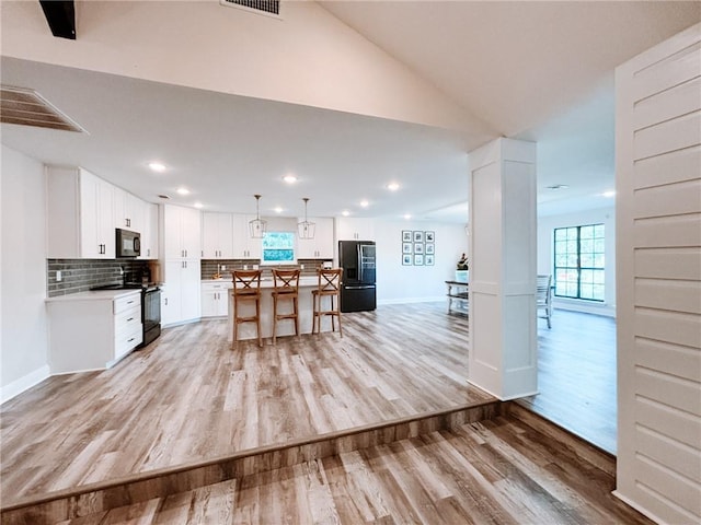 kitchen with open floor plan, a center island, tasteful backsplash, light wood finished floors, and black appliances