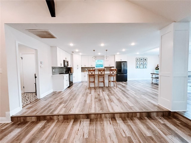 kitchen featuring a kitchen breakfast bar, a center island, light wood-type flooring, black appliances, and white cabinets