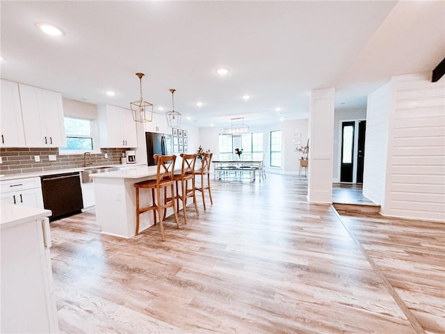 kitchen featuring backsplash, light hardwood / wood-style flooring, a kitchen island, dishwasher, and white cabinetry