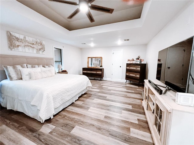 bedroom with light wood-type flooring, a raised ceiling, and ceiling fan