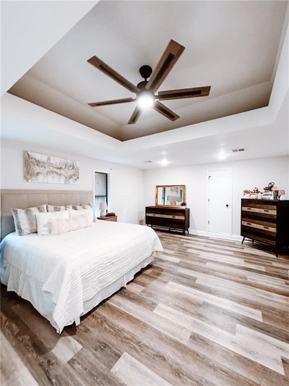 bedroom featuring light hardwood / wood-style flooring, ceiling fan, and a raised ceiling