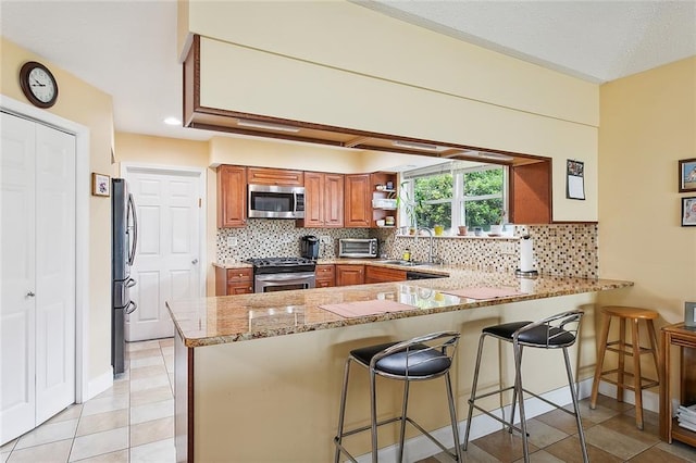 kitchen with light stone counters, a breakfast bar area, kitchen peninsula, and appliances with stainless steel finishes