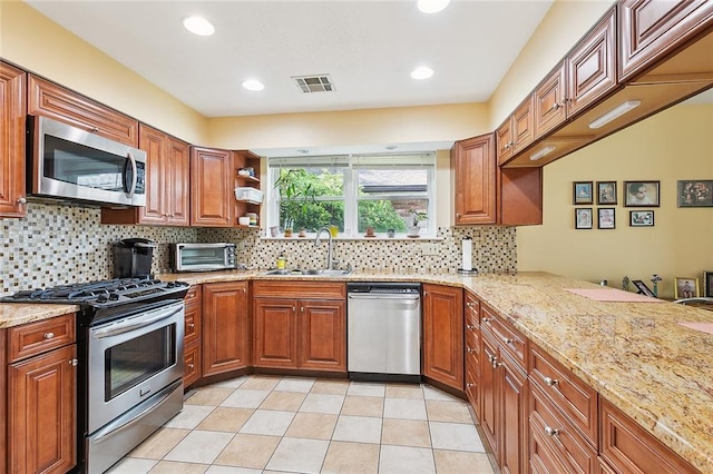 kitchen featuring appliances with stainless steel finishes, sink, light tile patterned floors, kitchen peninsula, and light stone countertops