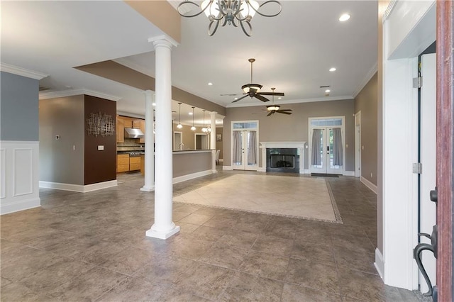 unfurnished living room with ceiling fan with notable chandelier, decorative columns, crown molding, and sink