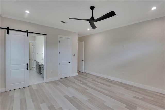 unfurnished bedroom with ensuite bathroom, a barn door, ceiling fan, light wood-type flooring, and crown molding