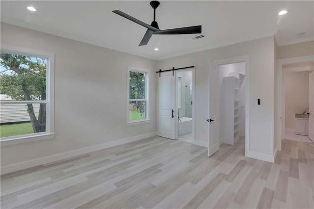 unfurnished bedroom featuring ceiling fan, a barn door, light wood-type flooring, a spacious closet, and a closet