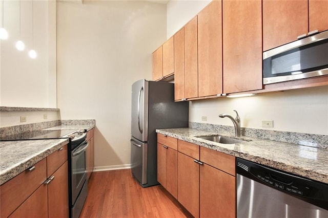 kitchen with sink, light stone countertops, stainless steel appliances, and light hardwood / wood-style floors