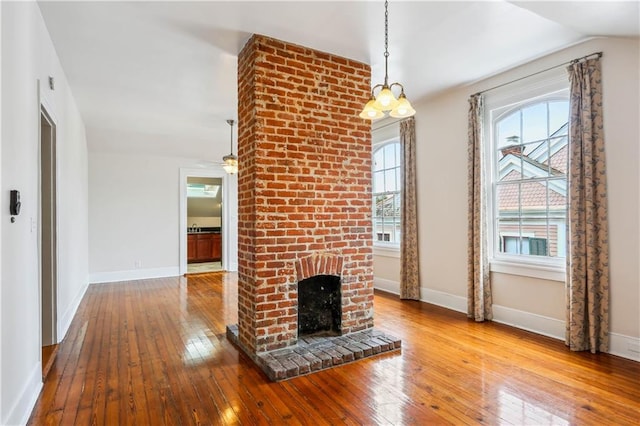 unfurnished living room with a chandelier, lofted ceiling, a brick fireplace, and light hardwood / wood-style flooring