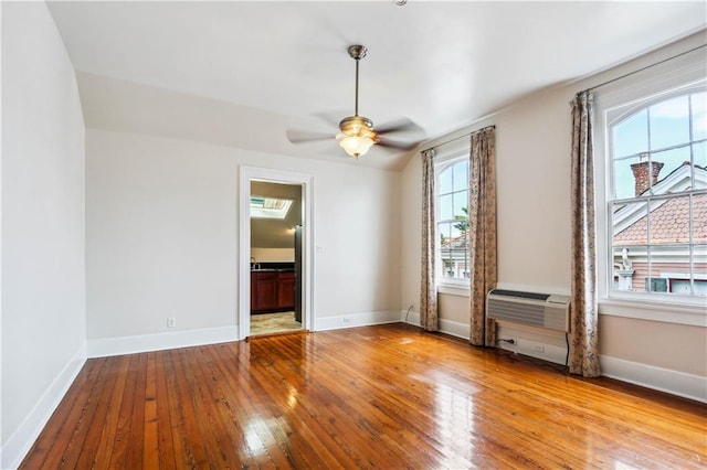 spare room with a wall unit AC, light hardwood / wood-style floors, ceiling fan, and a skylight