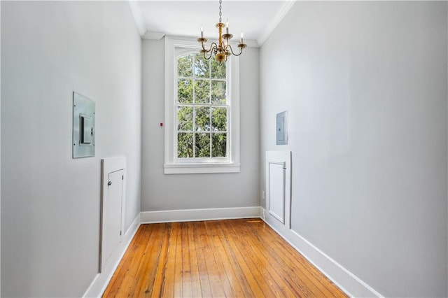 empty room with electric panel, light hardwood / wood-style floors, a chandelier, and crown molding