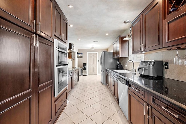 kitchen featuring appliances with stainless steel finishes, hanging light fixtures, light tile patterned floors, sink, and dark stone counters