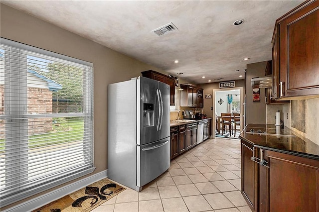 kitchen featuring dark stone countertops, sink, stainless steel fridge, light tile patterned floors, and black electric cooktop