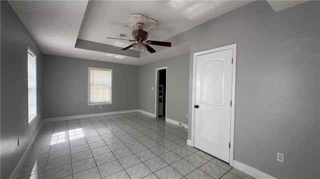 tiled empty room featuring a tray ceiling, a textured ceiling, ceiling fan, and a healthy amount of sunlight