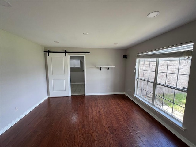 unfurnished room with baseboards, dark wood-type flooring, and a barn door