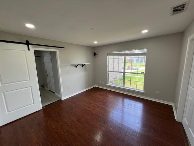 unfurnished bedroom with visible vents, a barn door, baseboards, and wood finished floors