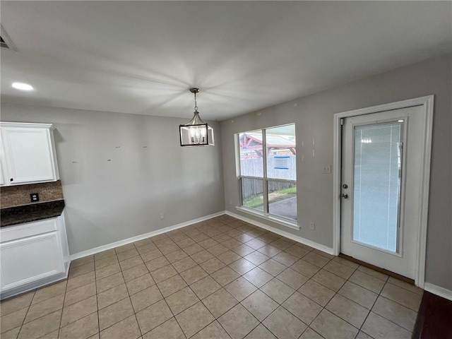 unfurnished dining area with light tile patterned floors, baseboards, and a notable chandelier