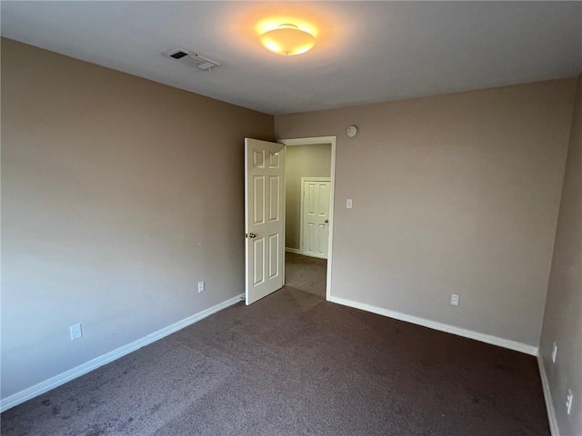 spare room featuring visible vents, baseboards, and dark carpet