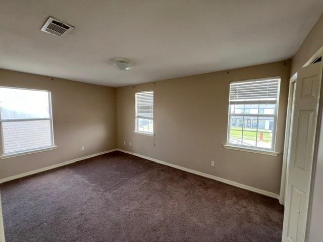 spare room with baseboards, visible vents, and dark carpet