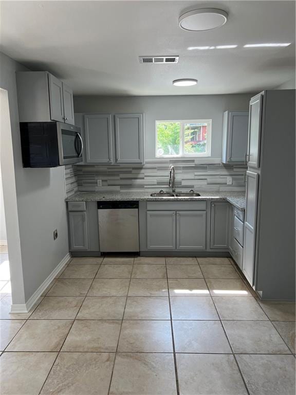 kitchen with light stone counters, tasteful backsplash, sink, gray cabinetry, and appliances with stainless steel finishes