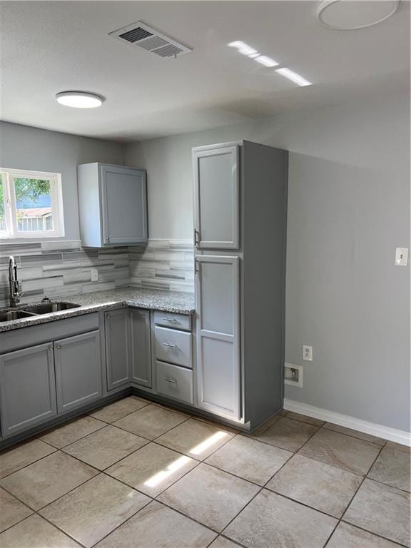 kitchen featuring sink, gray cabinetry, backsplash, stainless steel appliances, and light stone countertops