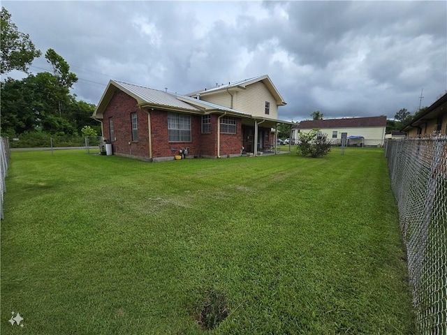 rear view of house with a yard, a fenced backyard, metal roof, and brick siding