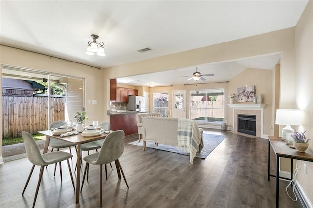 dining area featuring dark hardwood / wood-style floors, ceiling fan, vaulted ceiling, and a tiled fireplace