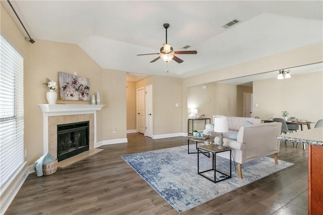 living room with a tiled fireplace, ceiling fan, dark wood-type flooring, and vaulted ceiling